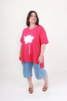 Woman wearing a pink t-shirt with a white flower design and blue shorts on a white background