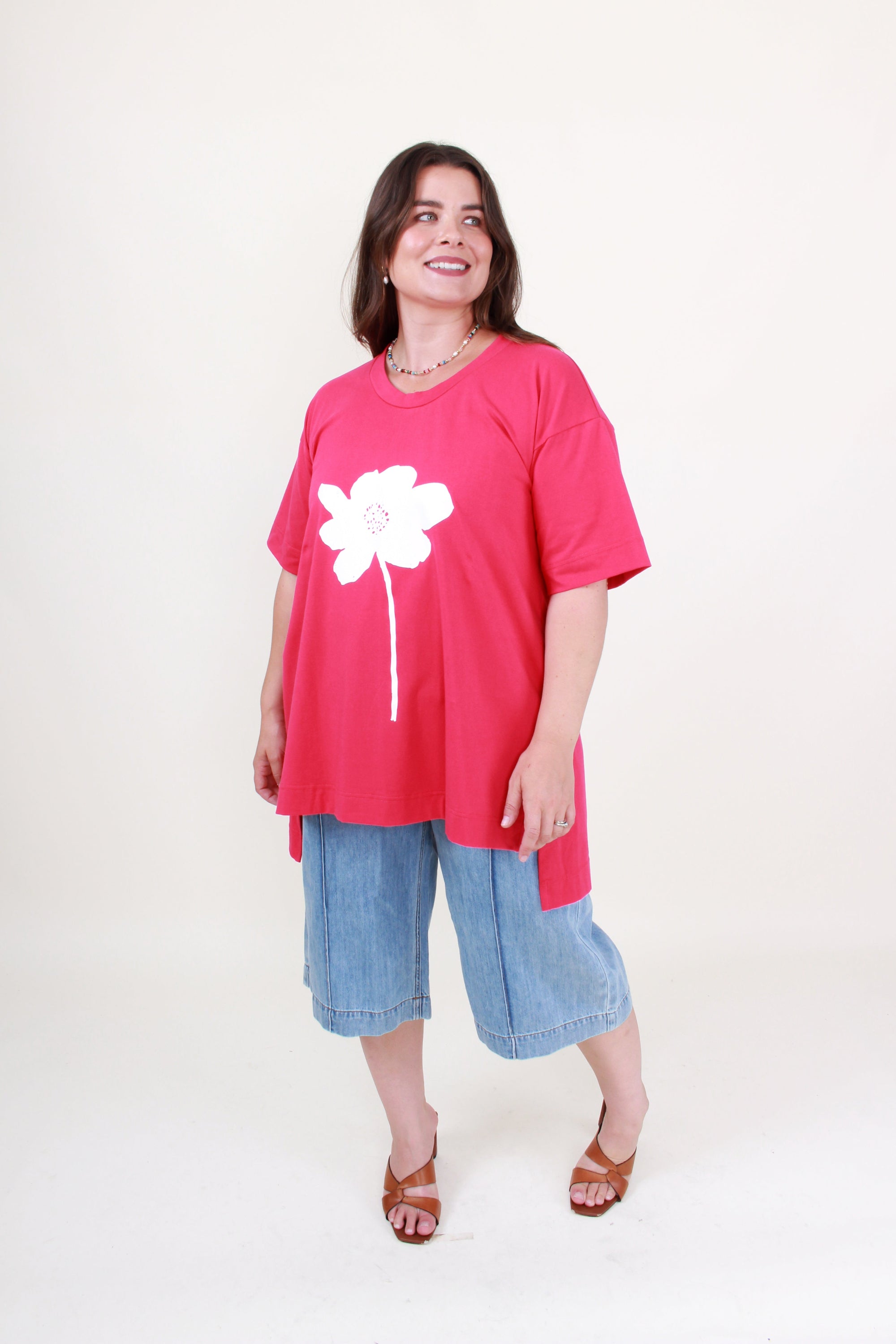 Woman wearing a pink t-shirt with a white flower design and blue shorts on a white background