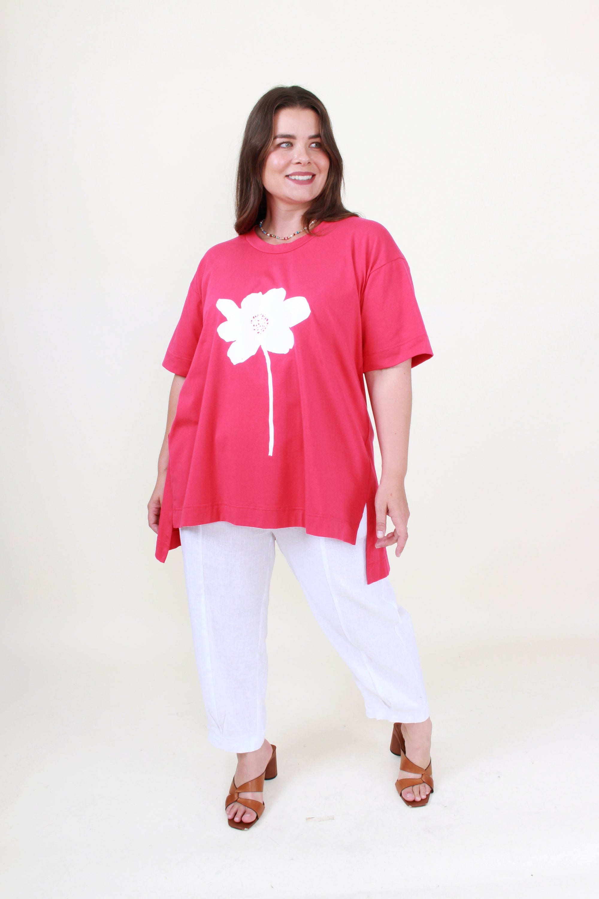 Woman wearing a pink tunic with a white flower design on a plain background