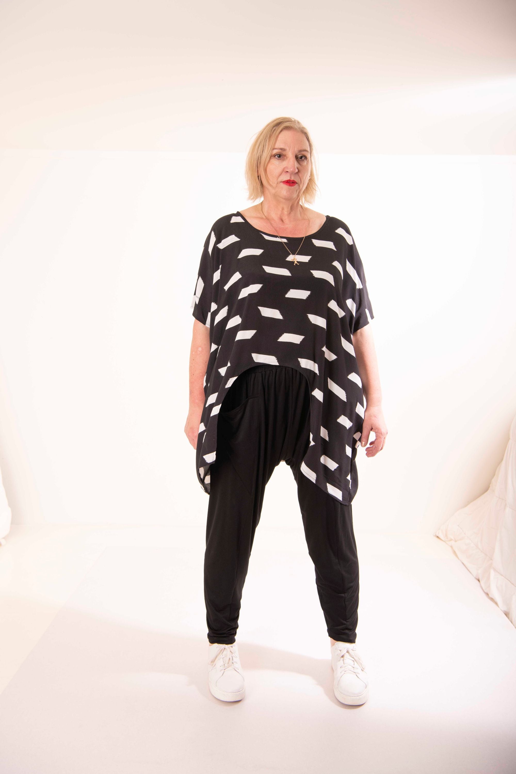 Woman wearing a black and white patterned top and black pants on a white background