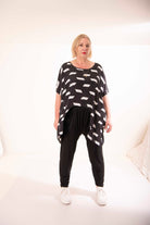 Woman wearing a black and white patterned top and black pants on a white background