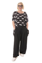 Woman wearing a black and white patterned top and black wide-leg pants on a white background