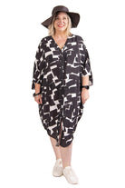 Woman wearing a black and white patterned kaftan with a wide-brimmed hat on a white background