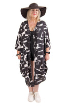 Woman wearing a black and white patterned kaftan and wide-brimmed hat on a white background.