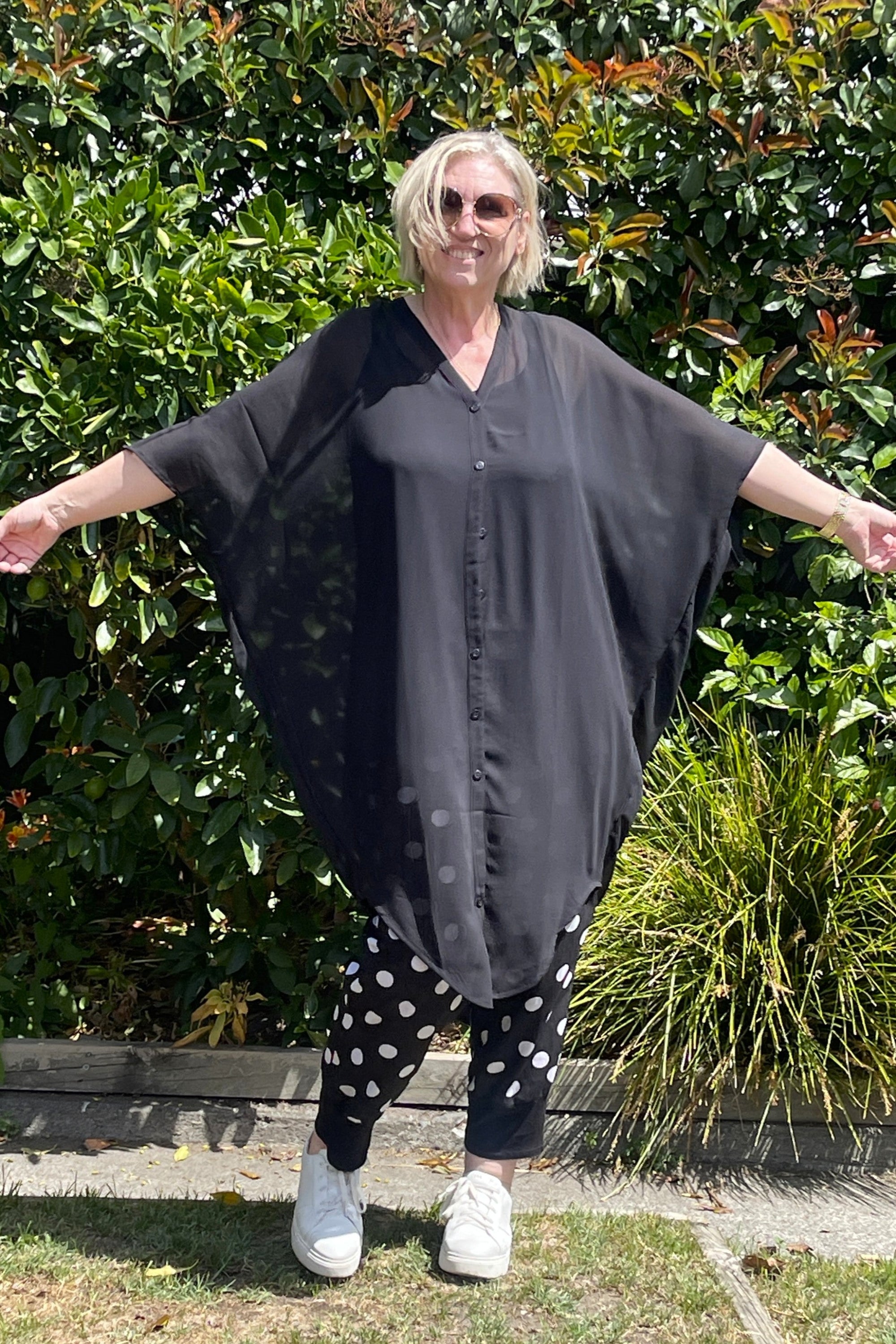 Woman wearing a black kaftan and hat standing in front of green bushes