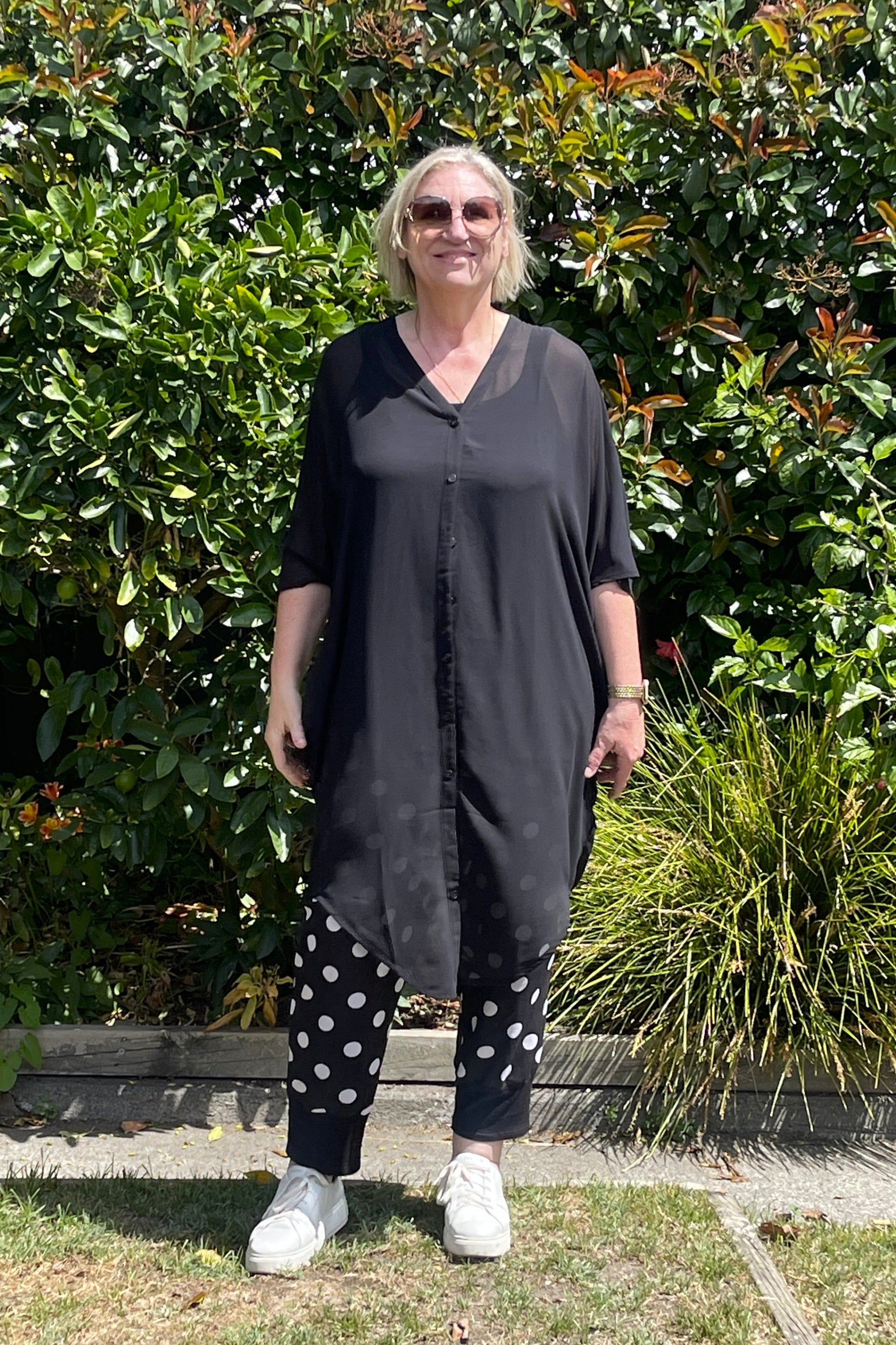 Woman wearing a black kaftan and hat standing in front of green bushes