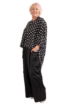 Woman wearing a black polka dot blouse and black wide-leg pants on a white background