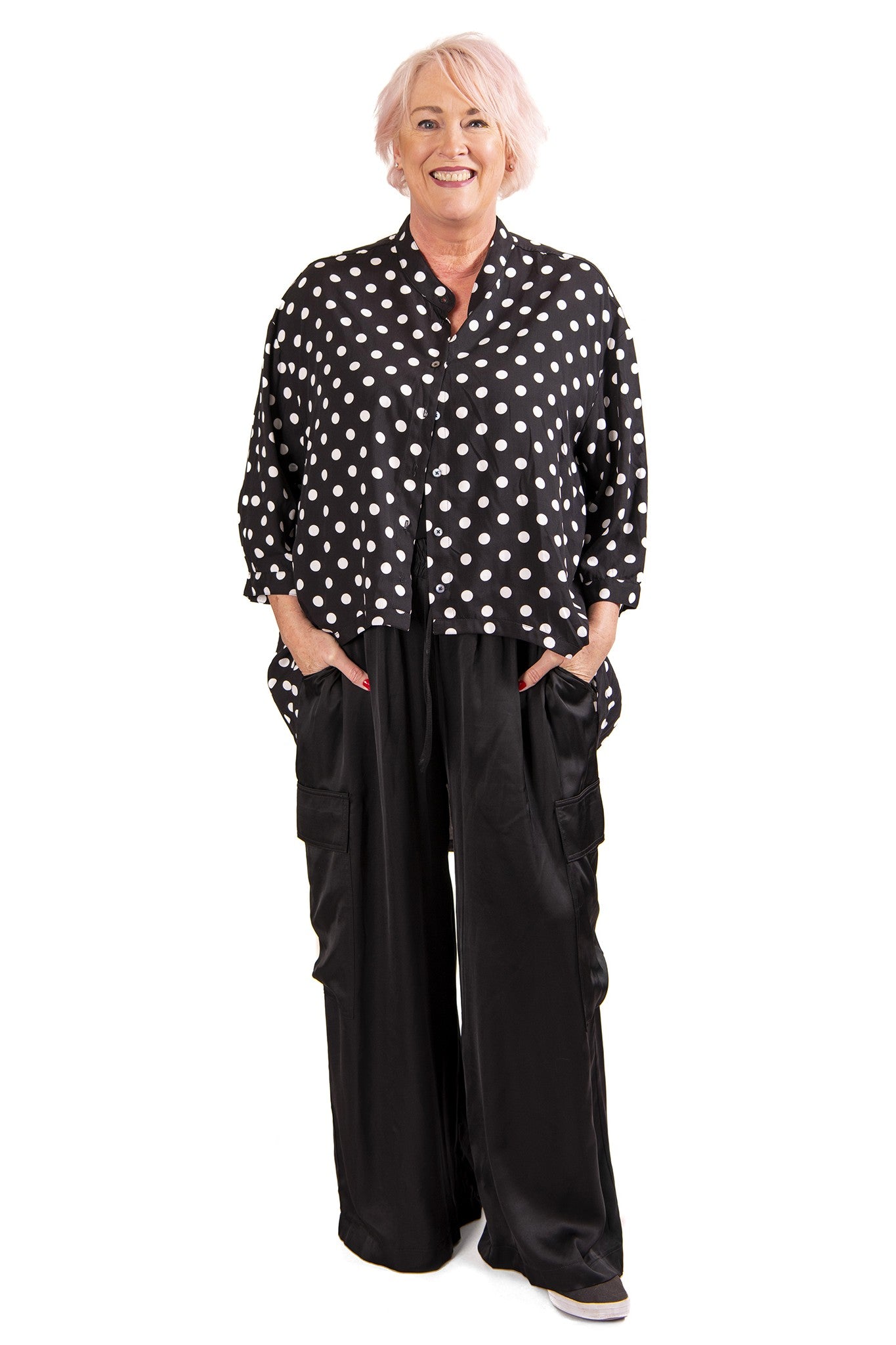 Woman wearing a black polka dot blouse and black wide-leg pants on a white background
