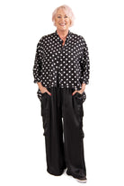 Woman wearing a black polka dot blouse and black wide-leg pants on a white background