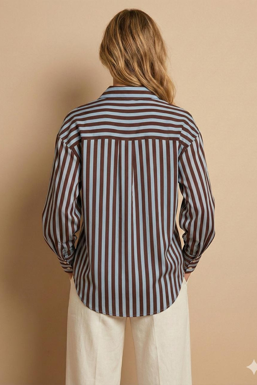 A woman viewed from behind wearing a long-sleeve button-up shirt with vertical brown, beige, and gray stripes, paired with cream-colored pants, set against a solid beige background.
