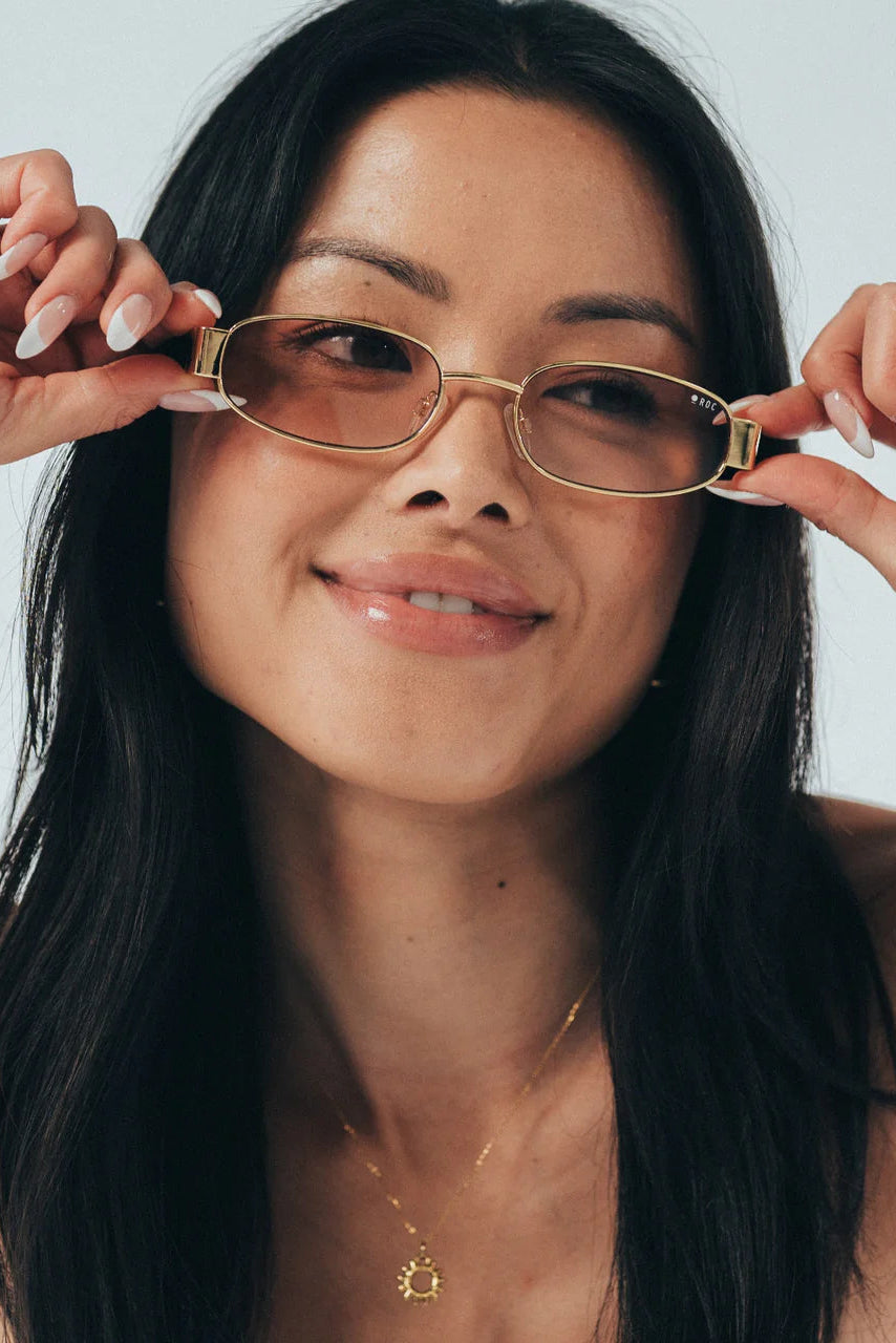 Woman holding gold-framed glasses up to her face against a plain background