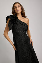 Woman wearing a black one-shoulder dress with a large bow on a gray background