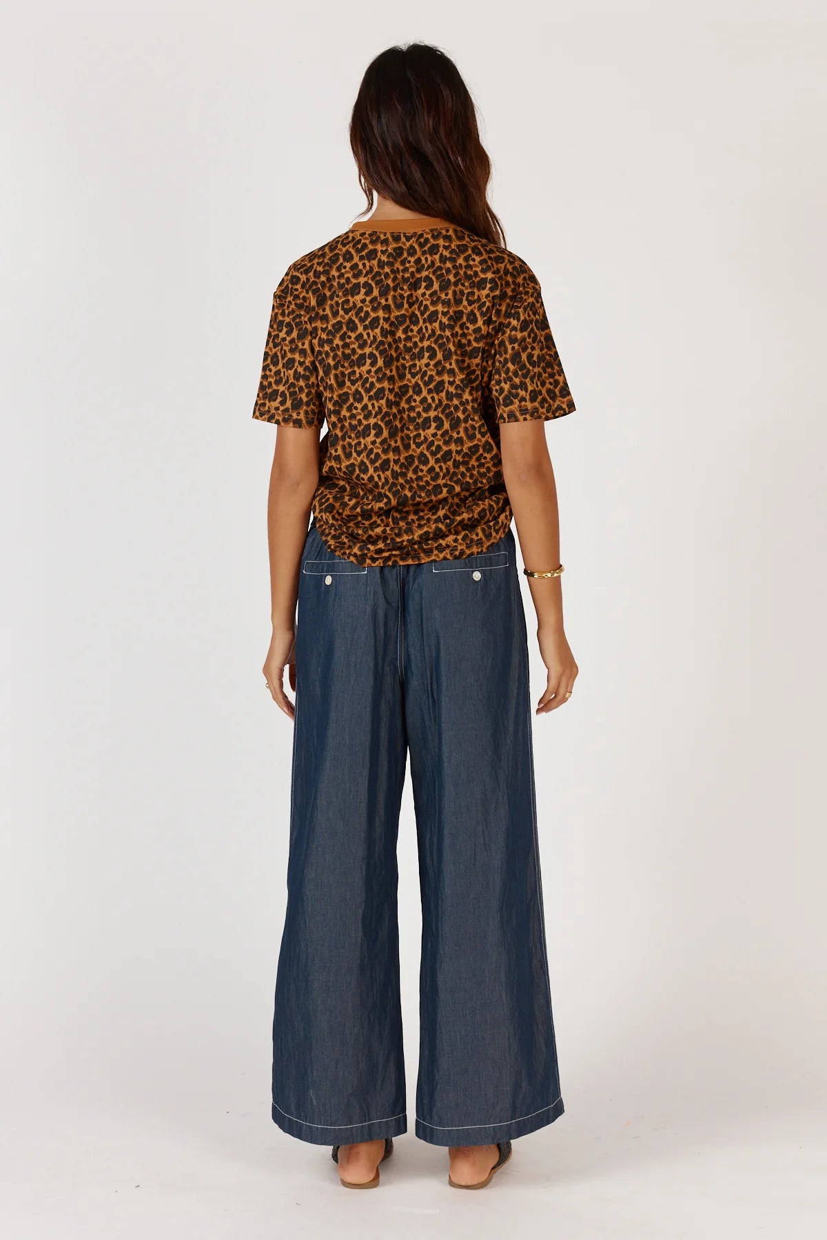 Person wearing a leopard print top and wide-leg jeans on a white background