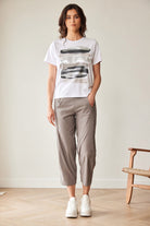 Woman wearing a white t-shirt with graphic design and beige pants standing in a minimalistic room.