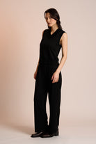 Woman wearing a black sleeveless top and pants against a beige background