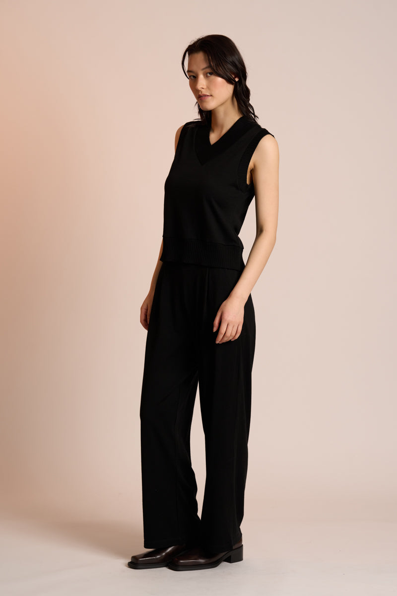 Woman wearing a black sleeveless top and pants against a beige background