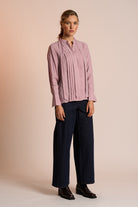 Woman wearing a dusty pink blouse and navy pants against a beige background