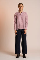 Woman wearing a dusty pink blouse and navy pants against a beige background