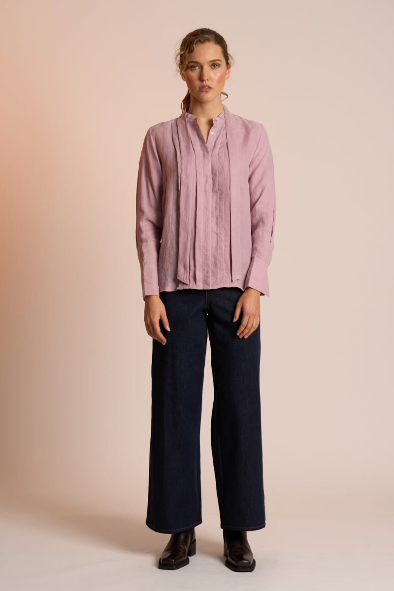 Woman wearing a dusty pink blouse and navy pants against a beige background