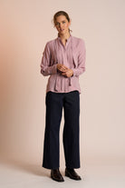 Woman wearing a dusty pink blouse and navy pants against a beige background