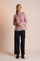Woman wearing a dusty pink blouse and navy pants against a beige background