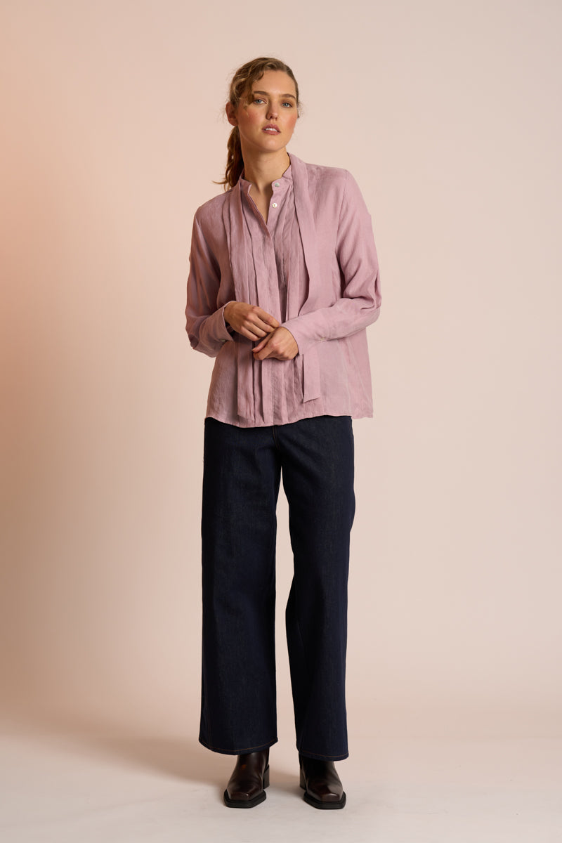 Woman wearing a dusty pink blouse and navy pants against a beige background