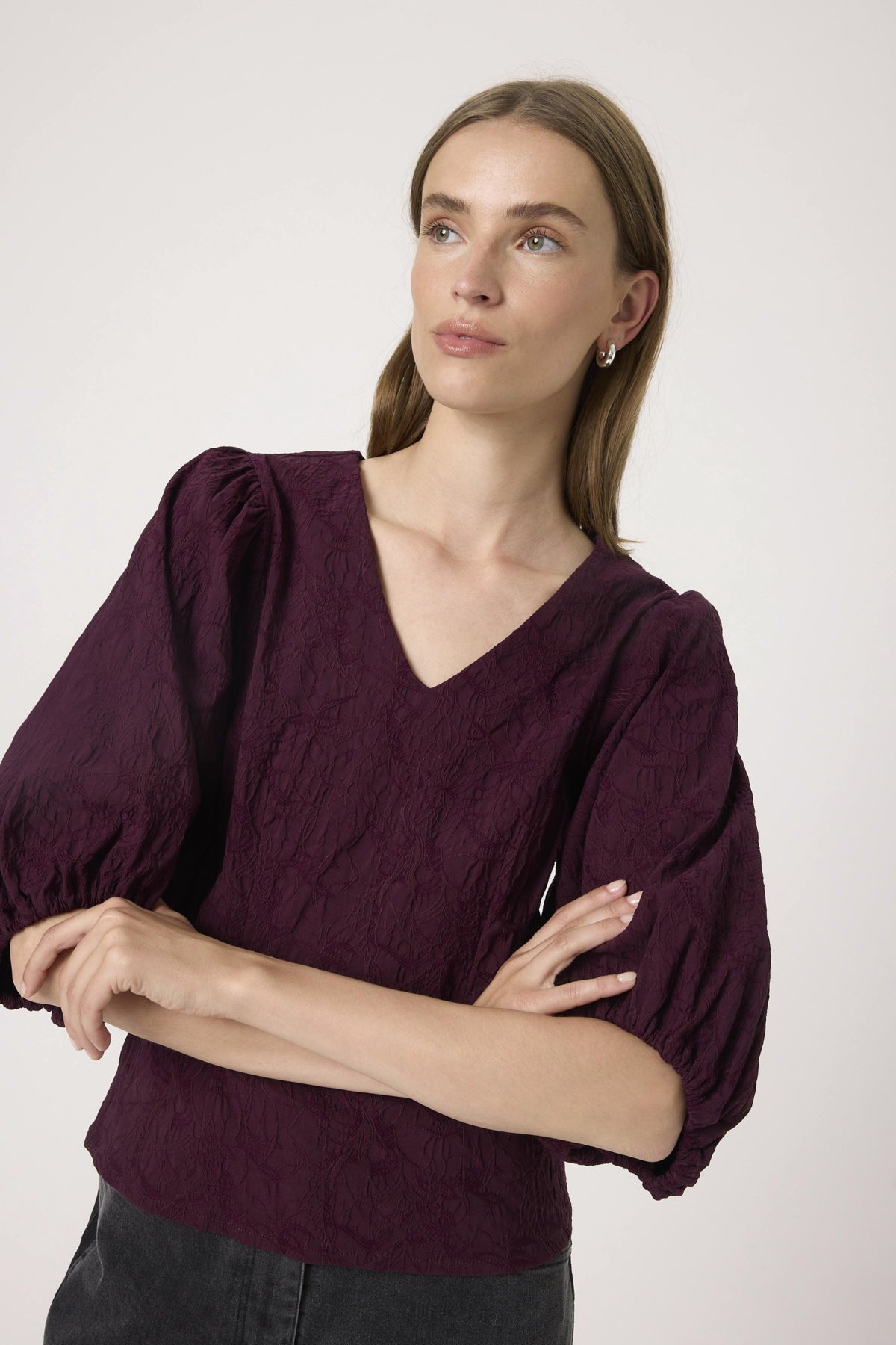 Woman wearing a burgundy blouse with puffed sleeves against a white background