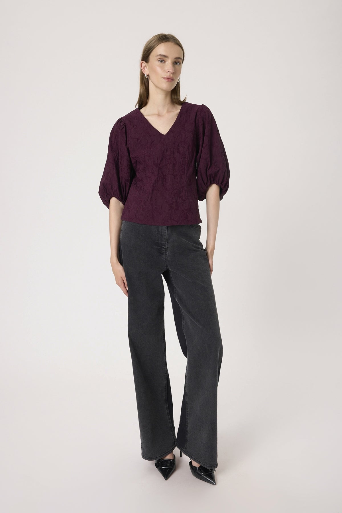 Woman wearing a burgundy top and black pants on a white background