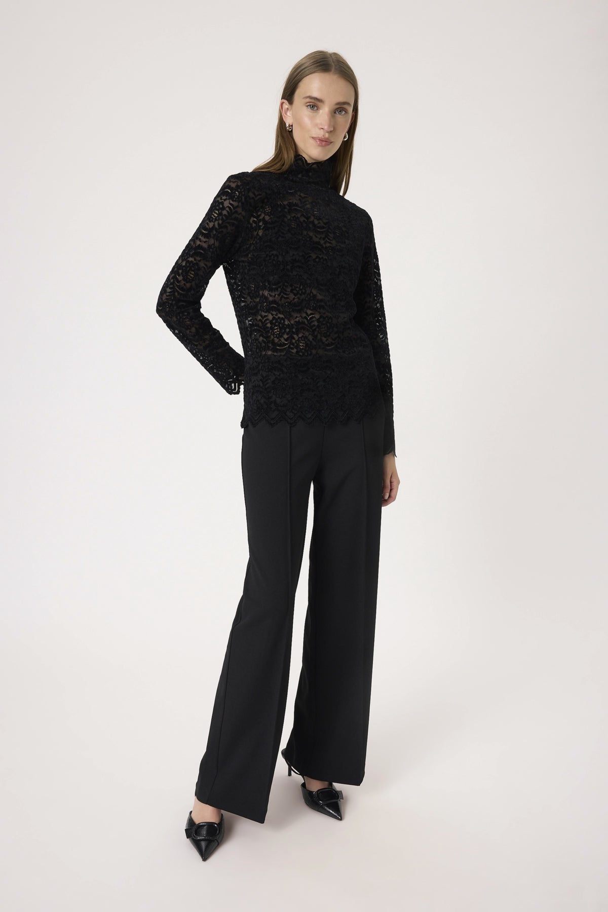 Woman wearing a black lace top and black pants on a white background