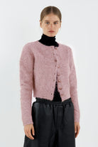 Person wearing a pink cardigan over a black turtleneck and pants on a white background