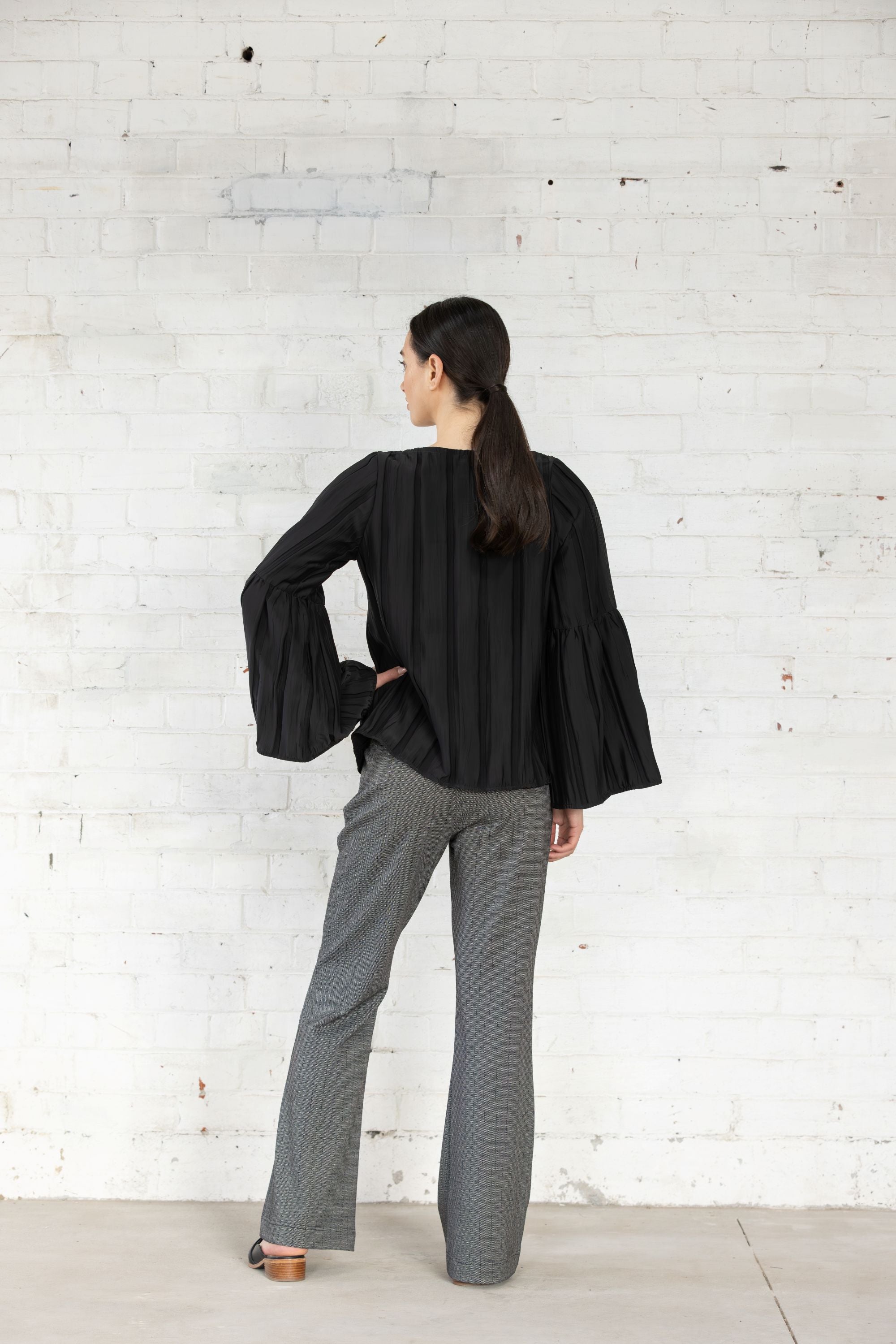 Person wearing a black outfit with gray pants against a white brick wal back view