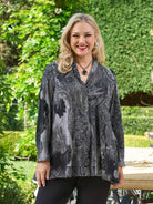 Woman wearing a patterned jacket outdoors with greenery in the background