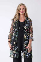 A woman modeling a sheer black floral kimono cardigan with three-quarter sleeves over a black top, photographed against a plain light gray studio background.