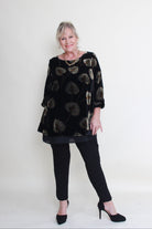 Woman wearing a black patterned top and black pants against a white background