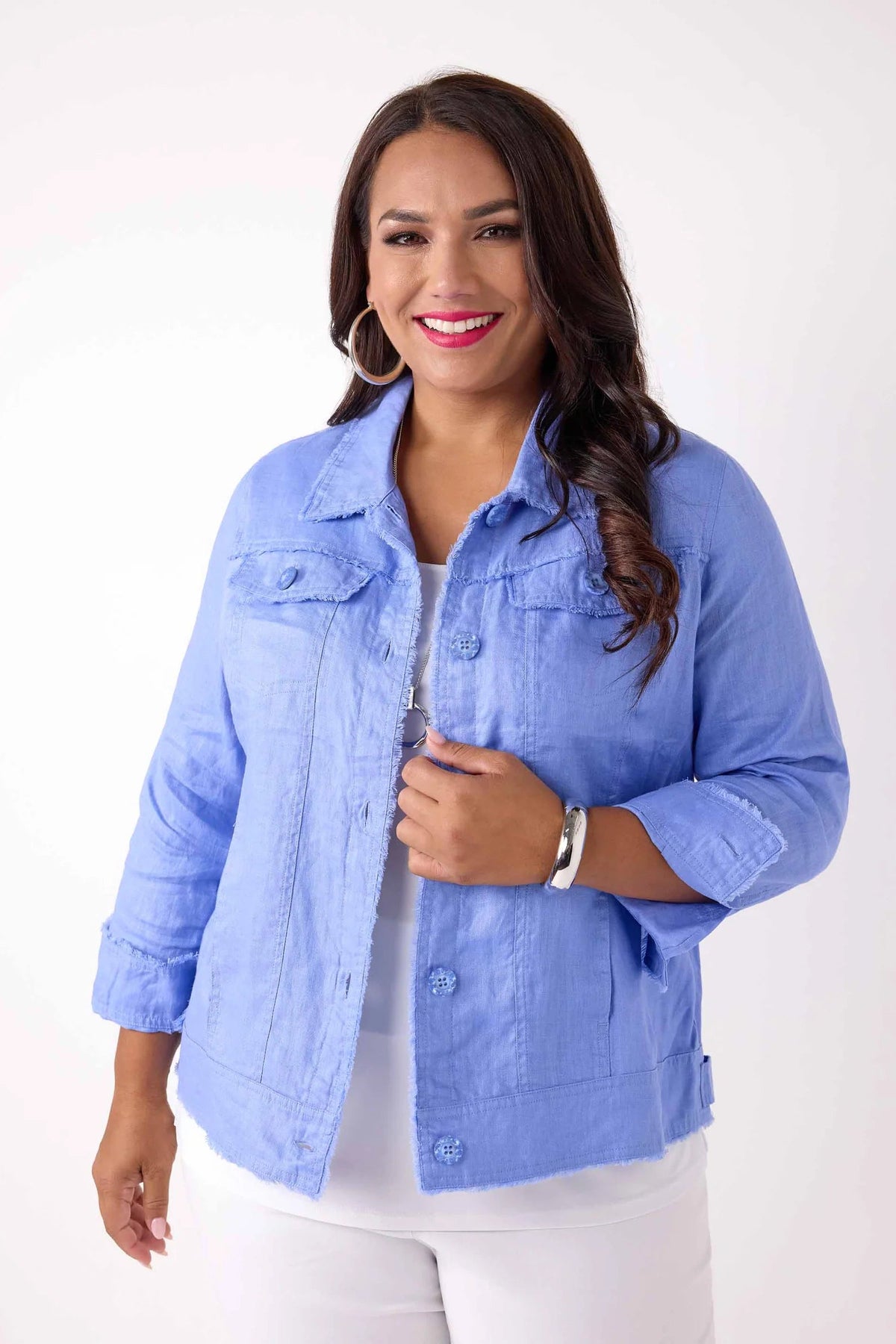 A woman modeling a light blue cropped denim jacket over a white top and white pants, standing against a plain white studio background.