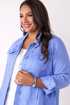 A woman wearing a light blue button-up shirt over a white top, photographed against a plain white studio background.