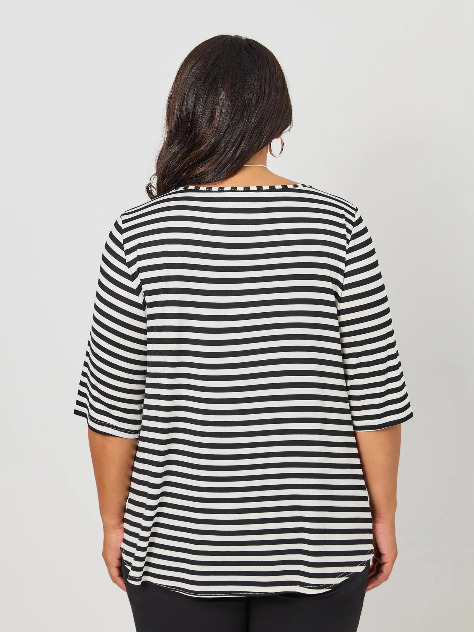 A woman viewed from the back wearing a black and white horizontally striped short-sleeve top, set against a plain light gray studio background.