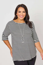 A woman modeling a black and white horizontally striped short-sleeve top with a boat neckline, paired with black pants and a long silver necklace, against a light gray studio background.