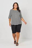 A woman modeling a black and white horizontally striped short-sleeve top with black knee-length shorts and black sandals, standing against a light gray studio background.
