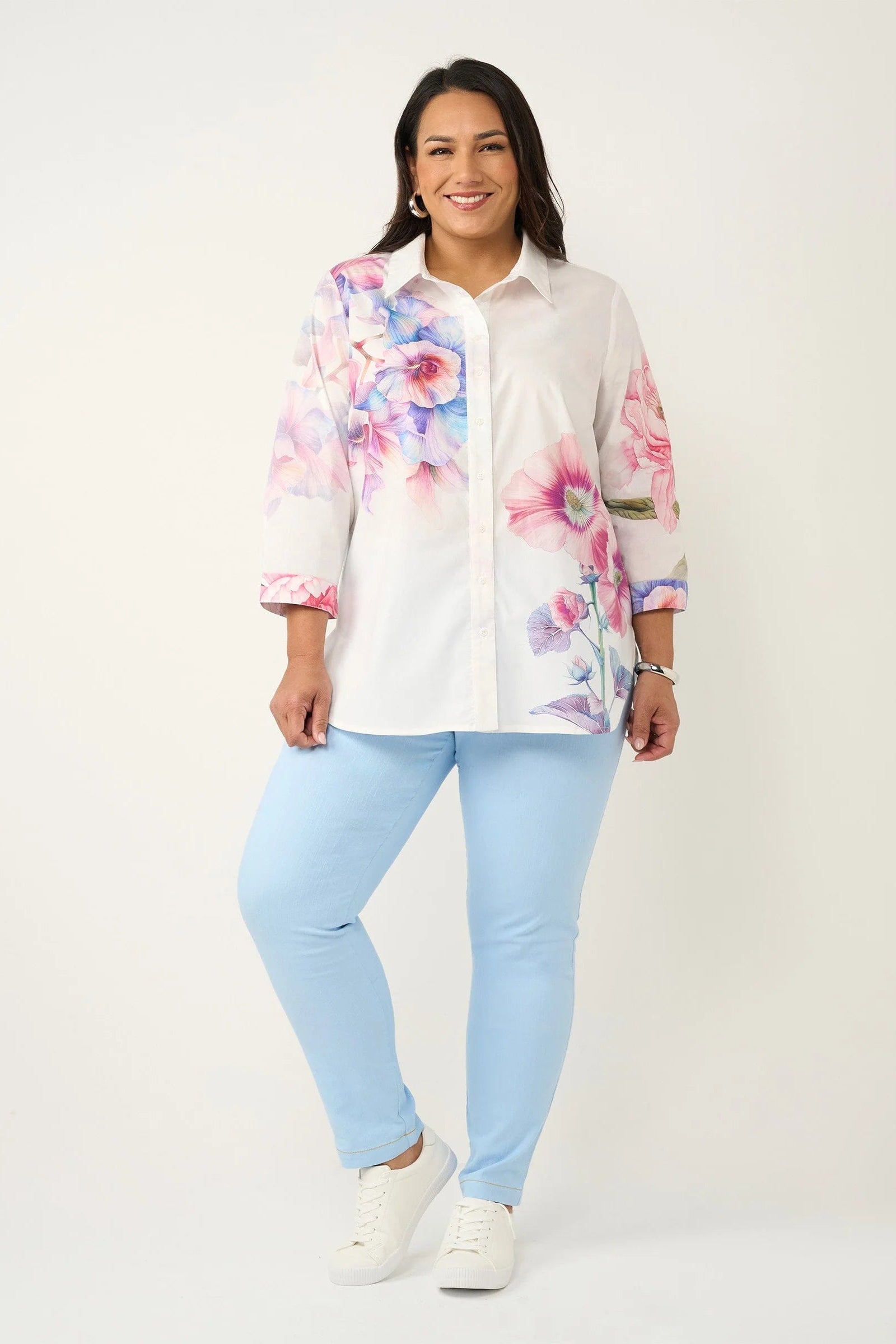 Woman wearing a floral blouse and light blue pants on a white background