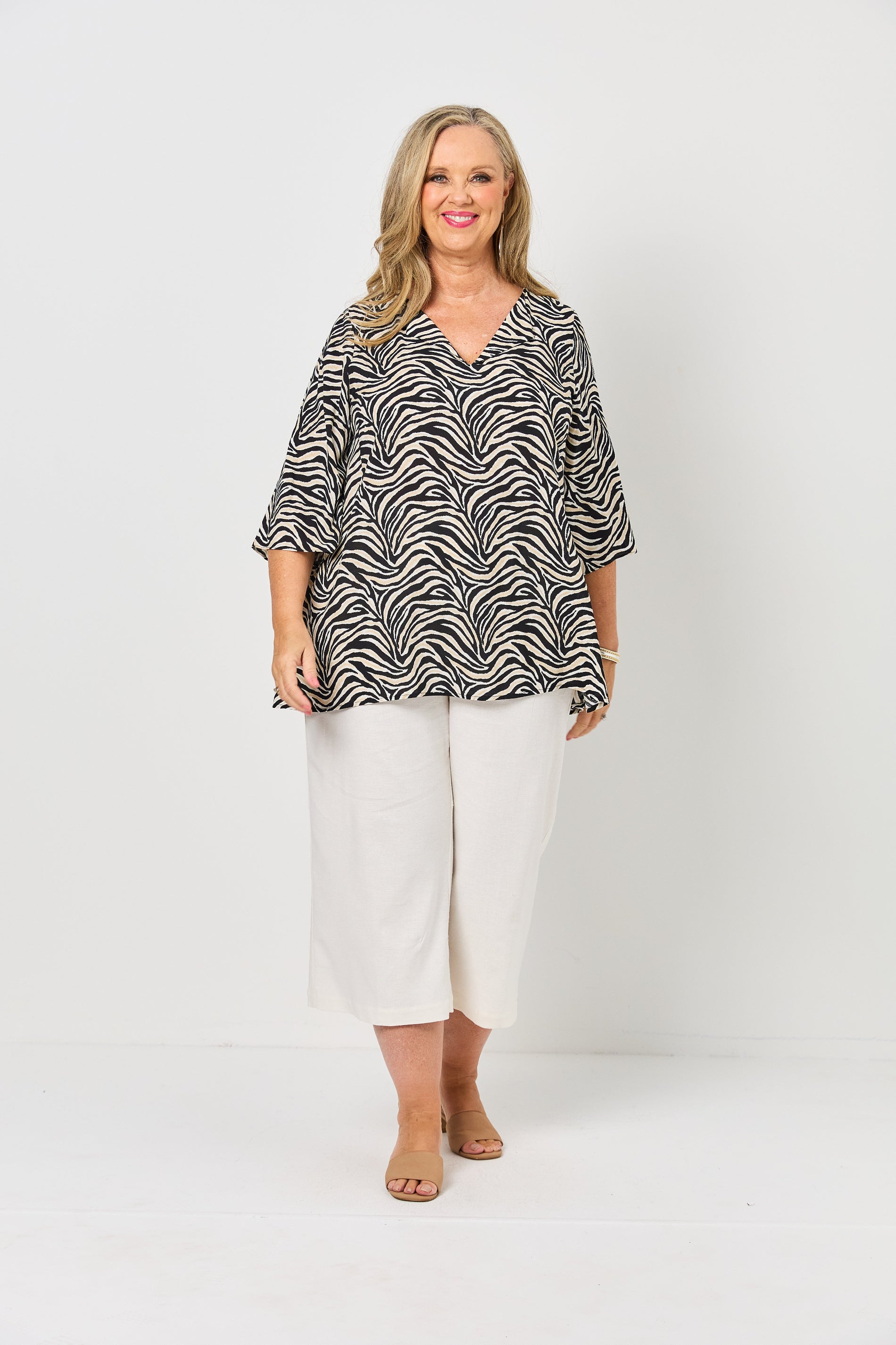 Woman wearing a black and white patterned top with white pants on a white background