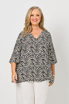 Woman wearing a black and white patterned top with white pants on a white background