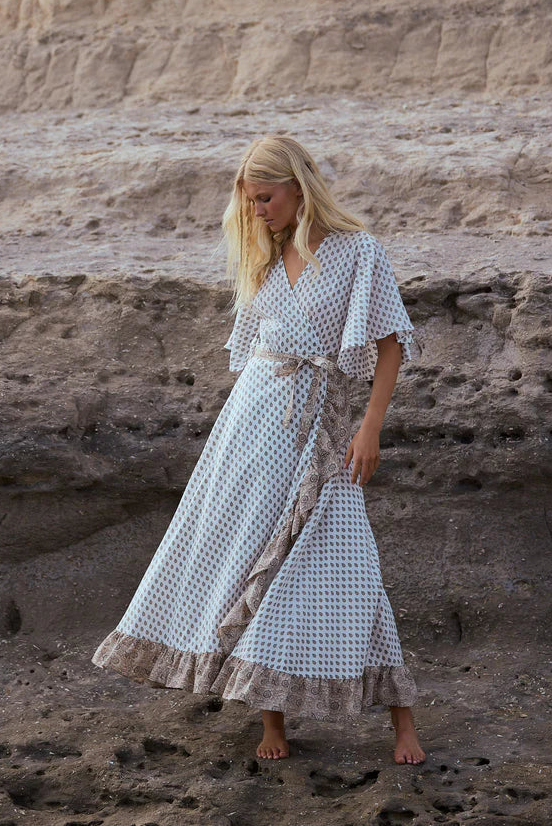 Woman in a long dress standing on rocky terrain with a cliff in the background
