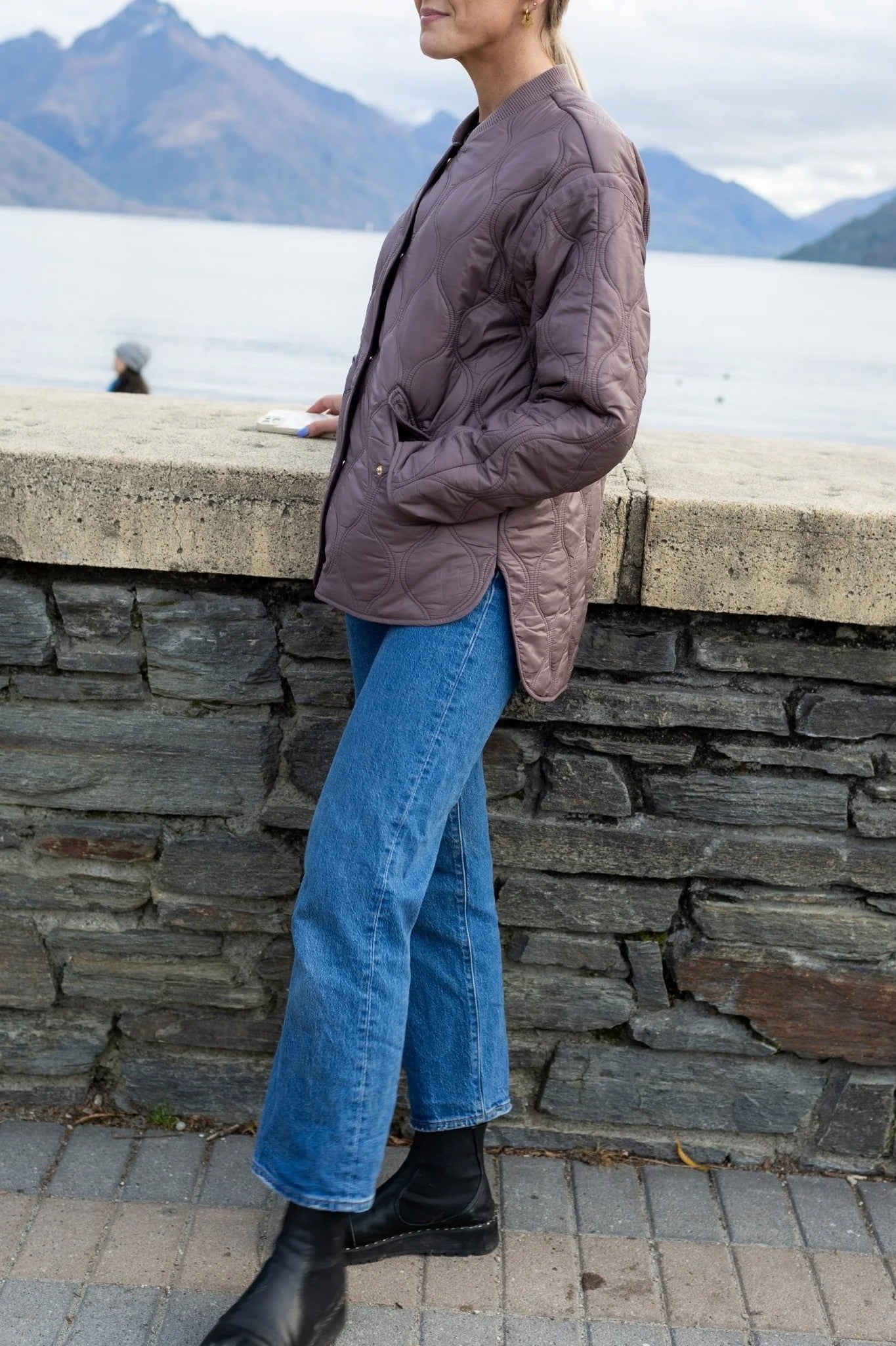 Woman wearing mauve brown quilted bomber and jeans in mountain setting