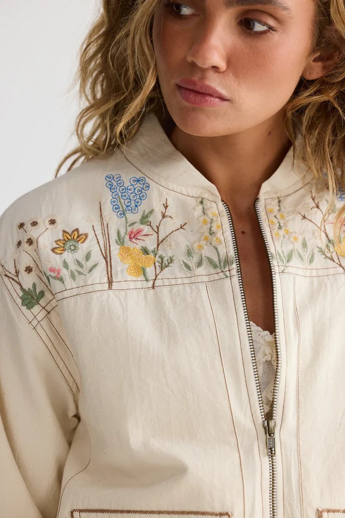 Close-up of a person wearing a beige jacket with floral embroidery on a plain background