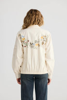 Person wearing a cream-colored jacket with floral embroidery on the back against a white background