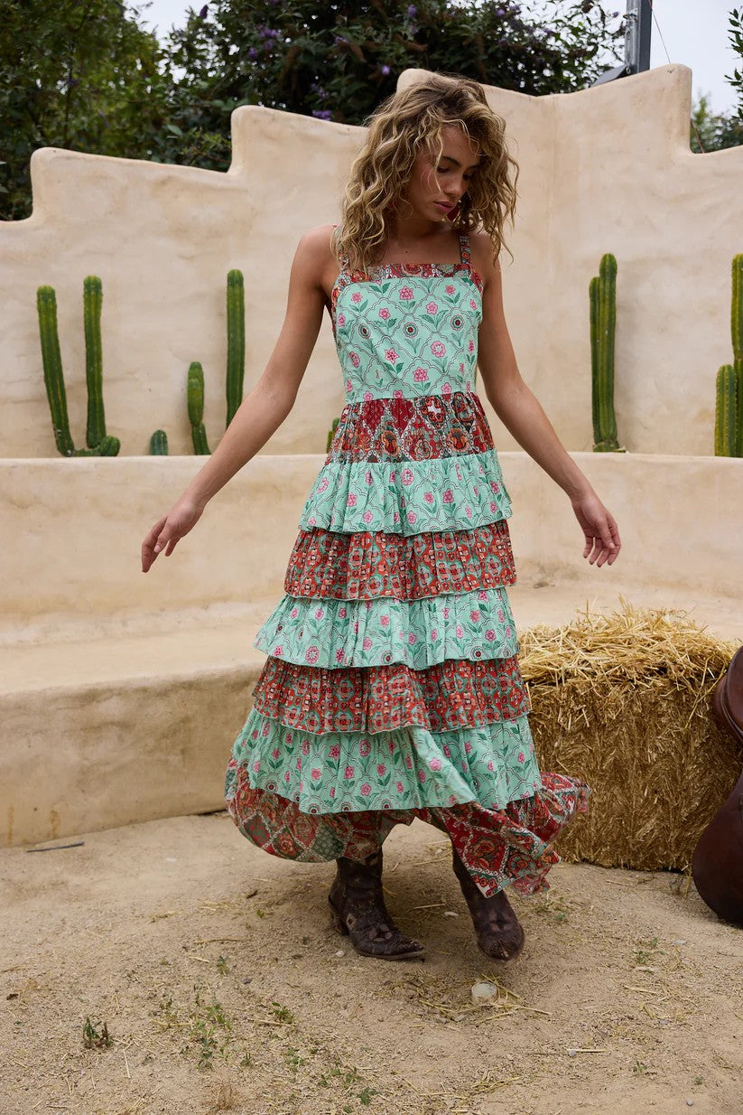 Woman wearing a floral tiered dress standing in front of a desert-like setting with cacti.