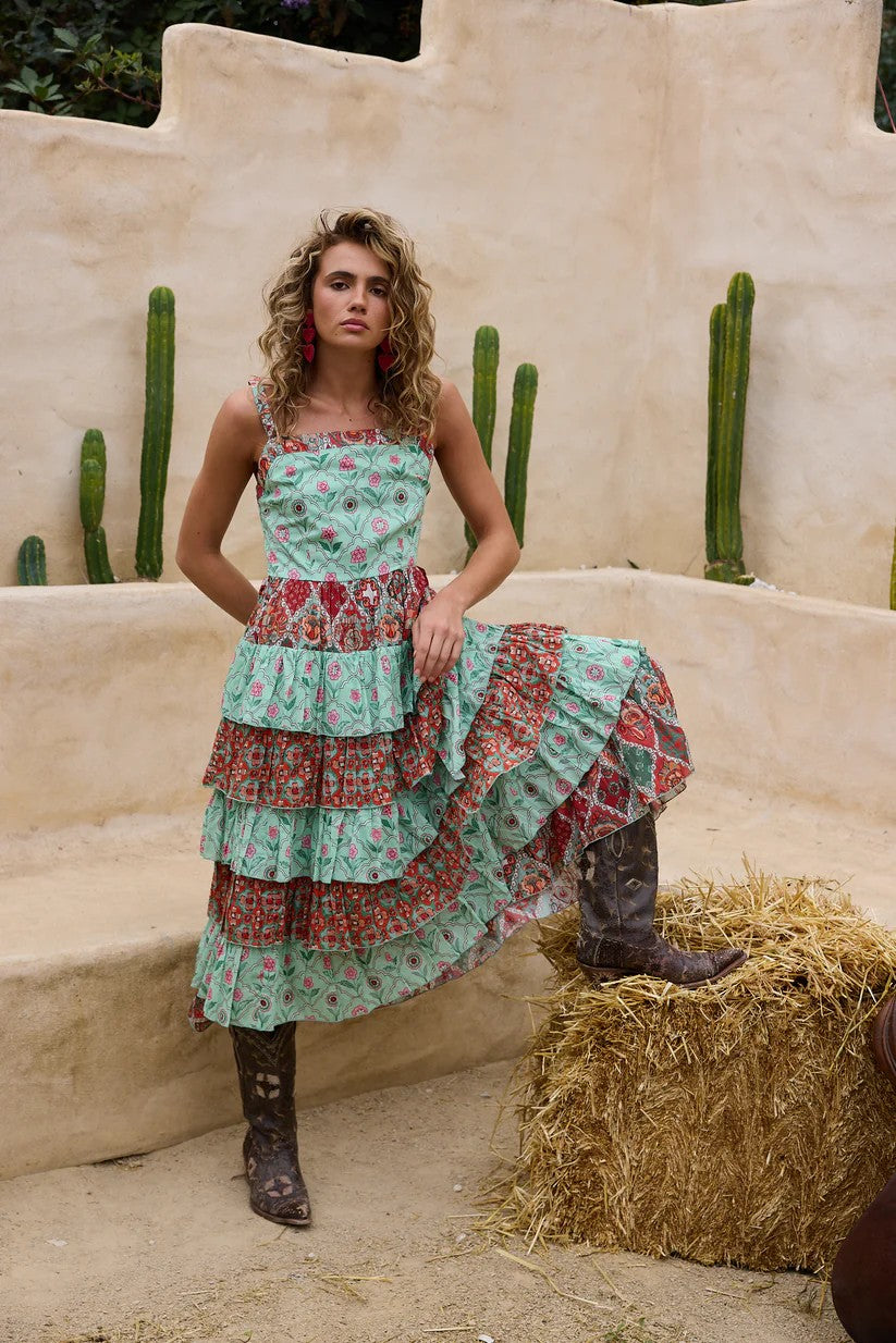Woman in a floral dress standing in a desert setting with cacti and hay.
