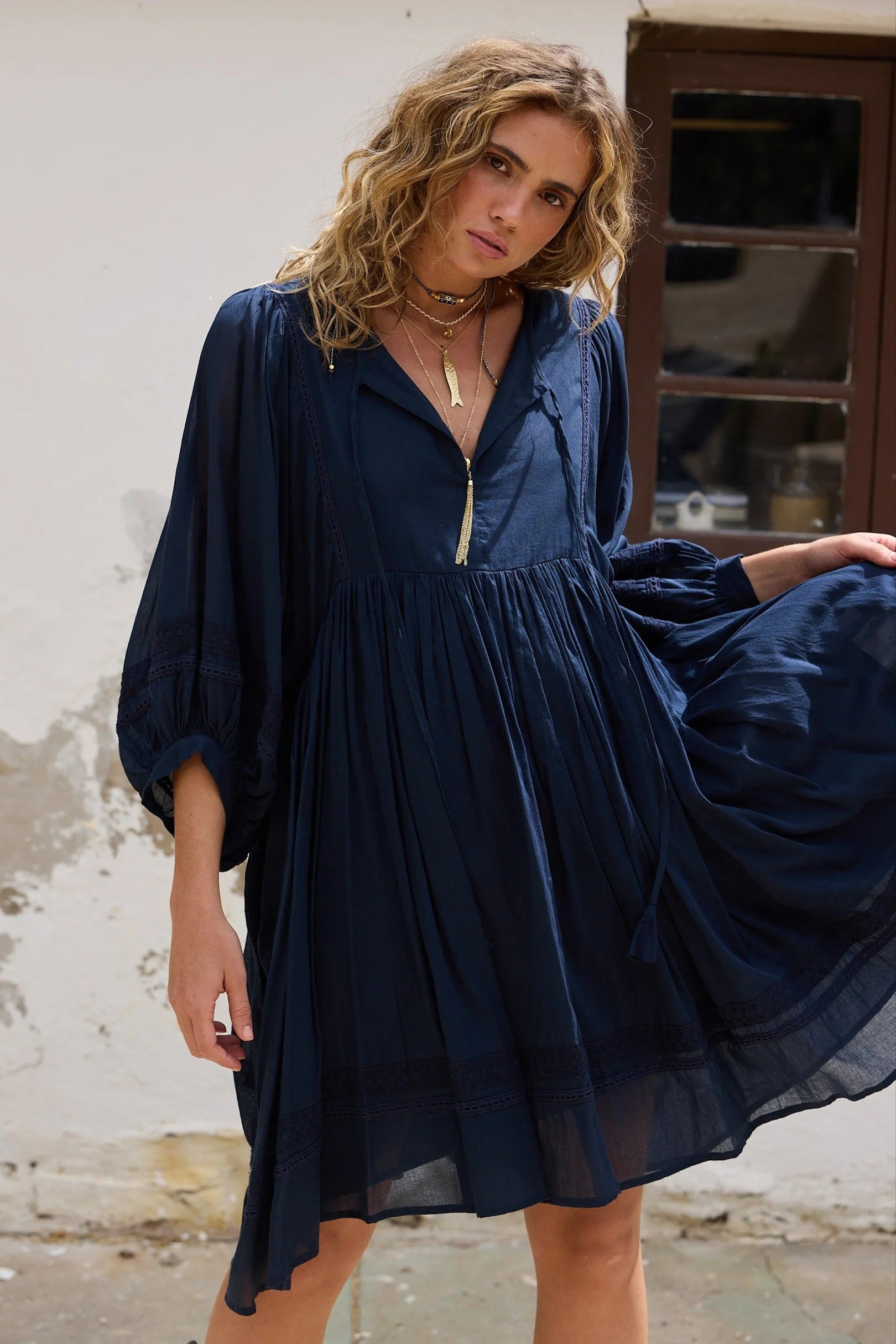 Woman wearing a blue dress standing against a textured wall.
