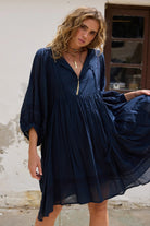 Woman wearing a blue dress standing against a textured wall.